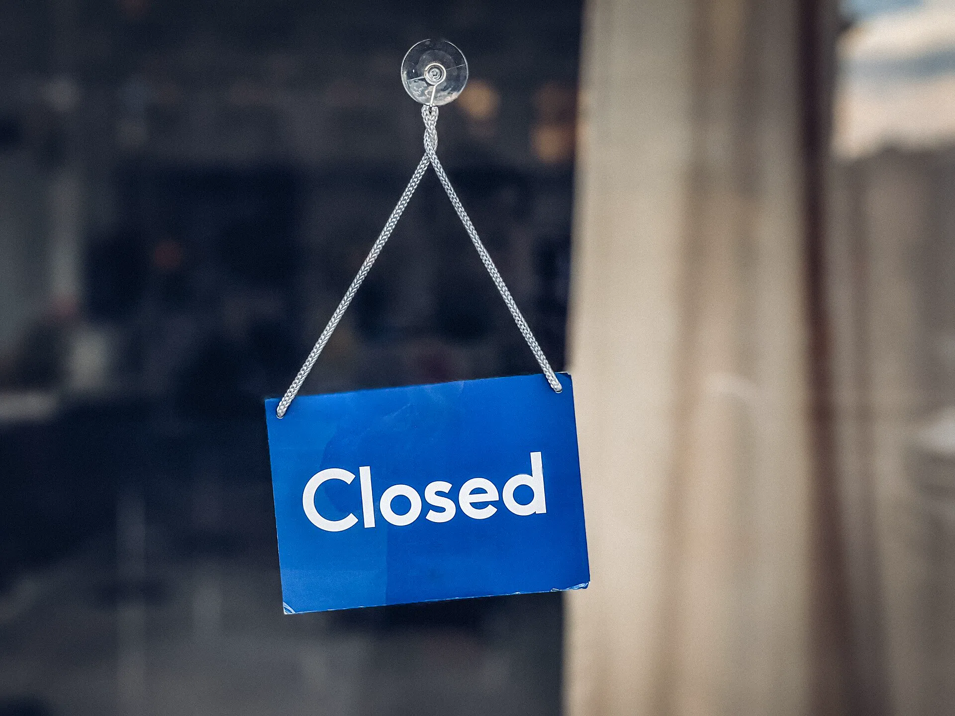 A blue Closed sign hanging on a cord inside a shop's glass door